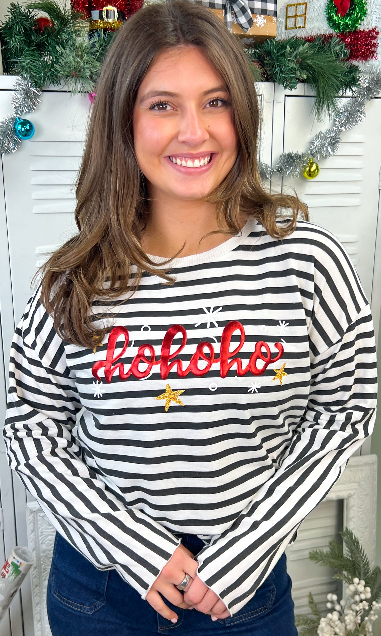 Model wearing the HoHoHo Christmas Metallic Puff Edgy LS Striped Graphic Shirt with festive decorations in the background.