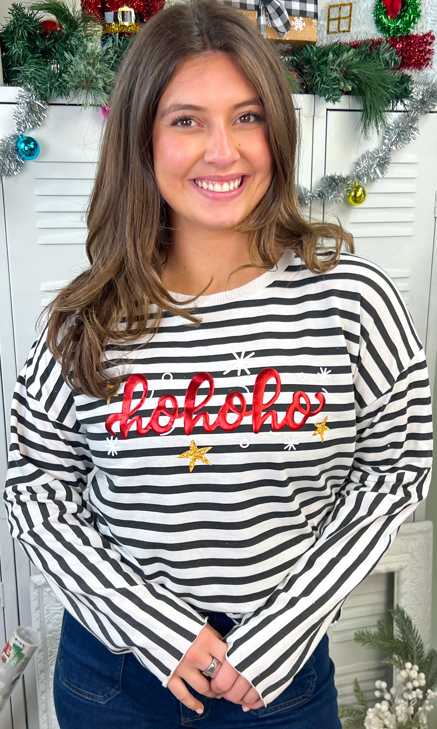 Model wearing the HoHoHo Christmas Metallic Puff Edgy LS Striped Graphic Shirt with festive decorations in the background.