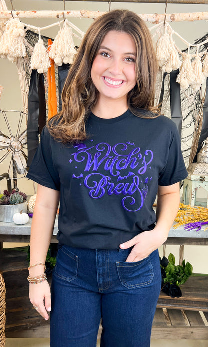 Stylish Witch's Brew Halloween Graphic Shirt featuring vibrant purple lettering, perfect for festive celebrations.